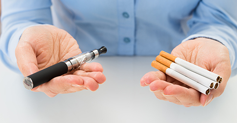 Person holding vape pen in one hand and cigarettes in the other.