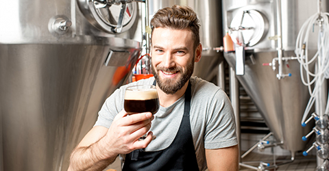 Brewer holding a dark beer in a glass smiling